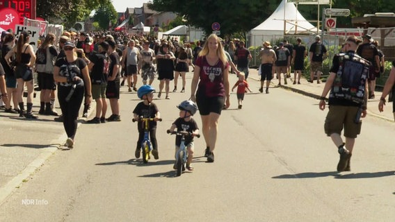 Zwei Kinder fahren auf Laufrädern über das Festivalgelände in Wacken. © Screenshot 