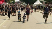 Zwei Kinder fahren auf Laufrädern über das Festivalgelände in Wacken. © Screenshot 