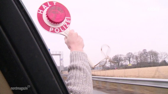 Eine rote Polizeikelle wird aus einem Autofenster gehalten. © Screenshot 