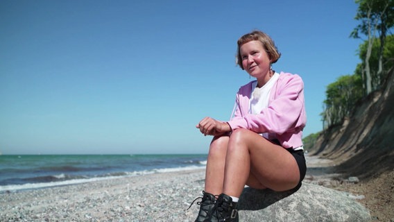 Caroline Wahl sitzt am Ostseestrand auf einem Stein. © Screenshot 
