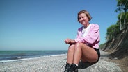 Caroline Wahl sitzt am Ostseestrand auf einem Stein. © Screenshot 
