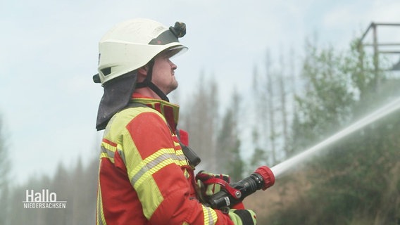 Ein Feuerwehrmann steht im Harzer Wald und richtet einen Wasserstrahl auf sein Ziel. © Screenshot 
