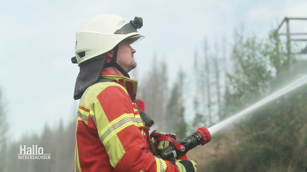 Ein Feuerwehrmann steht im Harzer Wald und richtet einen Wasserstrahl auf sein Ziel.