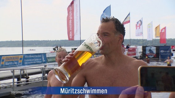 Ein Müritz-Schwimmer in Badehose trinkt nach seinem sportlichen Einsatz aus einem riesigen Bierglas. © Screenshot 