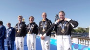 Das deutsche Triathlon-Staffel-Team um Lasse Lührs bei der Siegerehrung nach ihrem ersten Platz bei den Olympischen Spielen in Paris. © Screenshot 