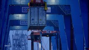 Ein Container wird von einem Kran in einem Hafen verladen. © Screenshot 