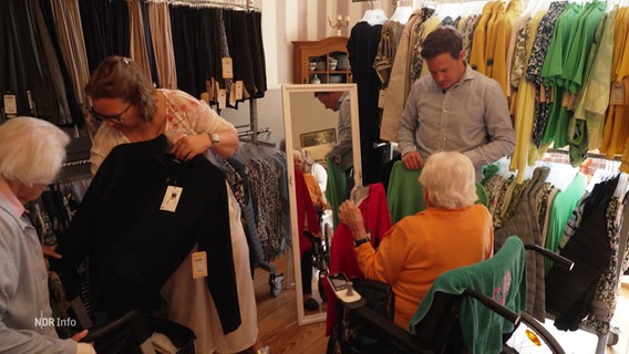 Zwei Seniorinnen schauen sich Kleider an, die von einer mobilen Modeboutique in ihr Seniorenheim gebracht wurden. © Screenshot 