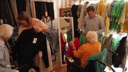 Zwei Seniorinnen schauen sich Kleider an, die von einer mobilen Modeboutique in ihr Seniorenheim gebracht wurden. © Screenshot 