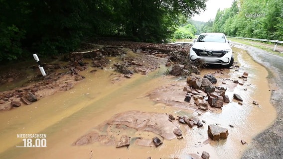 Wasser, Schlamm und Steine blockieren die Straße vor einem stehenden Auto. © Screenshot 