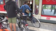 Mehrere Reisende mit Fahrrädern warten beim Einsteigen vor der Tür eines Regionalzuges. © Screenshot 
