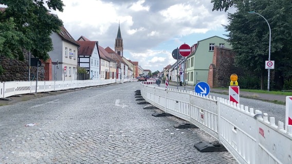 Sperrzäune stehen auf dem Kopfsteinpflaster der Zufahrtsstraße. © Screenshot 