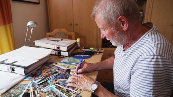 Sammler Bernd Möller an seinem Schreibtisch, auf dem viele Postkarten liegen. © Screenshot 
