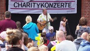 Ein Kinderliedermacher und ein kleines Mädchen stehen auf einer Bühne und singen bei einem Charity-Konzert. © Screenshot 