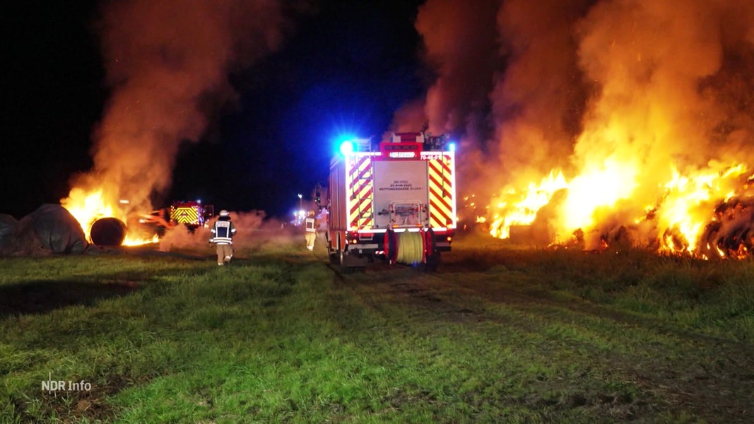 Ein Feuerwehrwagen steht auf einem Feld neben brennenden Heuballen.