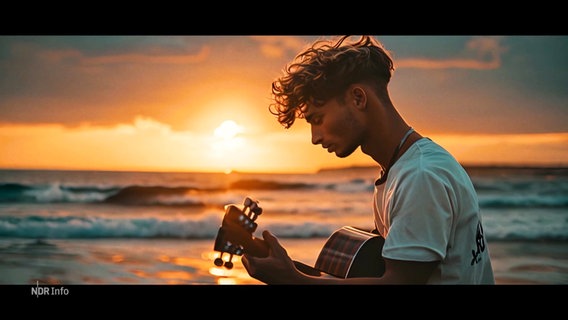 Eine mit KI generierte Animation zeigt einen jungen Mann, der am Strand im Sonnenuntergang Gitarre spielt. © Screenshot 