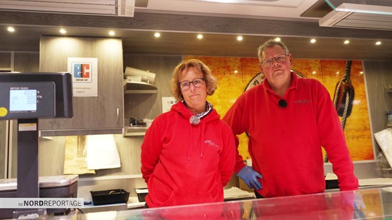 Eine Frau und ein Mann in roten Sweatshirts stehen in einem Fischverkaufswagen © Screenshot 