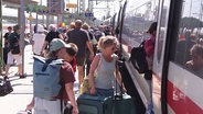 Viele Menschen mit Gepäck steigen in einen Zug ein. © Screenshot 