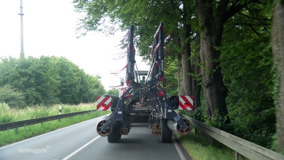 Ein Traktor mit einer Erntemaschine fährt auf einer Landstraße. © Screenshot 