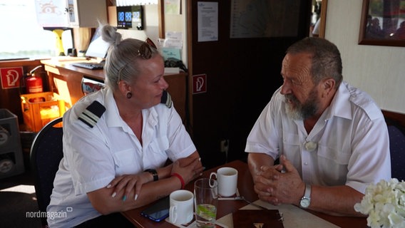 Ein Mann und eine Frau in Schiffs-Uniform sitzen an einem Tisch und trinken Kaffee. © Screenshot 