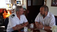 Ein Mann und eine Frau in Schiffs-Uniform sitzen an einem Tisch und trinken Kaffee. © Screenshot 