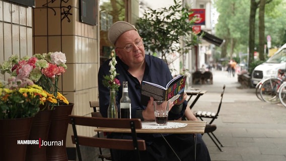 Daniel Plettenberg sitz an einem Tisch und liest ein Buch. © Screenshot 