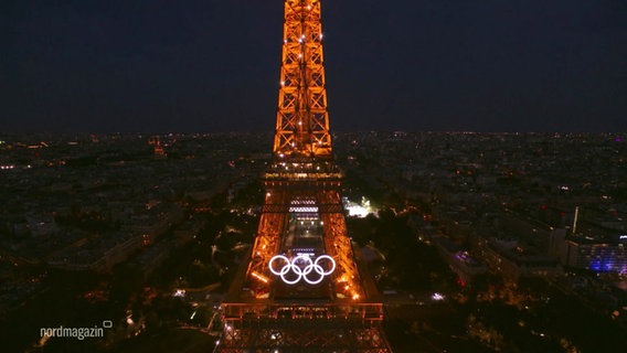 Der orange beleuchtete Eiffelturm mit dem Olympia Zeichen. © Screenshot 