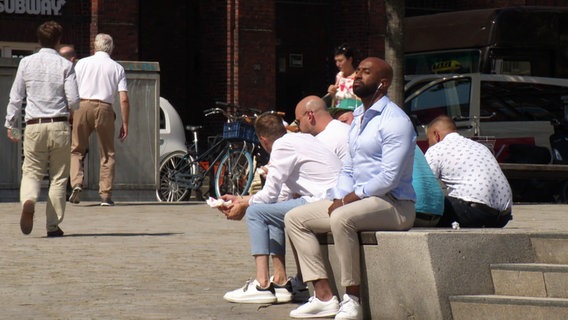 Ein Mann sitzt am Rand eines Brunnens und genießt die Sonnenstrahlen. © Screenshot 