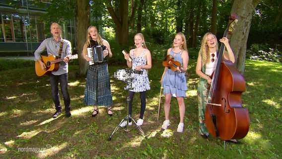 Vier junge Frauen und ein Herr stehen mit Musikinstrumenten im Grünen. © Screenshot 