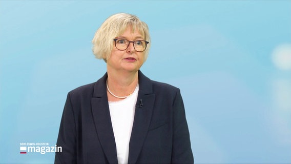 Ein blonde Frau mit Brille und blauem Blazer blickt in die Kamera. © Screenshot 