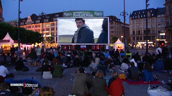 Mensche sitzen vor der Filmbühne am Hamburger Rathausmarkt. © Screenshot 