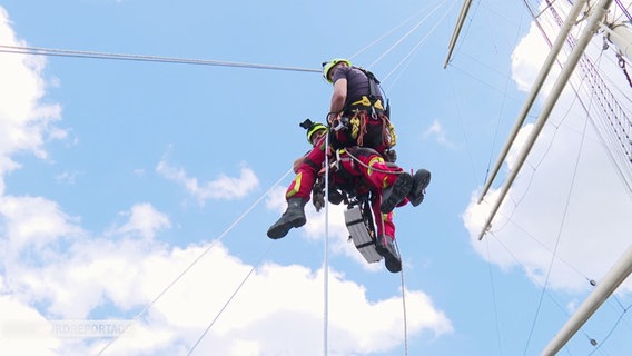 Ein Feuerwehrmann seilt sich vor blauem Himmel ab. © Screenshot 