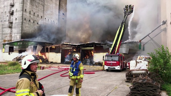 Feuerwehrleute löschen eine brennende Lagerhalle zwischen Getreidesilos. © Screenshot 