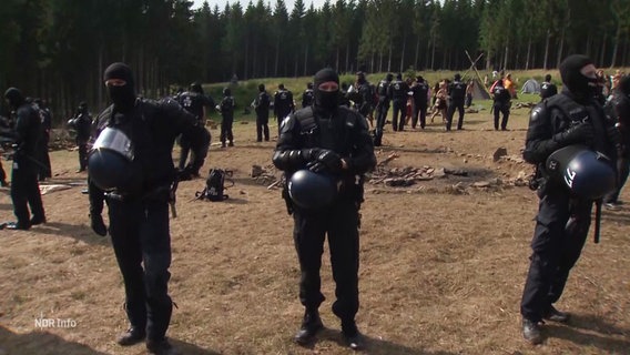 Mehrere Polizisten schirmen eine Feuerstelle ab. © Screenshot 