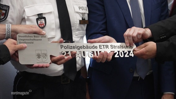 Polizeibeamte halten einen großen, symbolischen Schlüssel mit der Aufschrift "Polizeigebäude ETR Stralsund". © Screenshot 