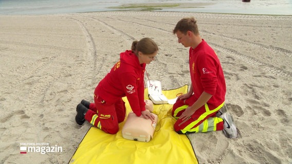 Zwei junge DLRG-Mitglieder zeigen am Strand wie die Reanimation mit einem Defibrilator funktioniert. © Screenshot 