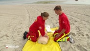 Zwei junge DLRG-Mitglieder zeigen am Strand wie die Reanimation mit einem Defibrilator funktioniert. © Screenshot 