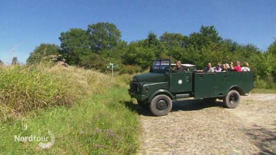 Ein Hanomag Fahrzeug mit Üassagieren auf der Ladeflläche fährt über einen Feldweg. © Screenshot 