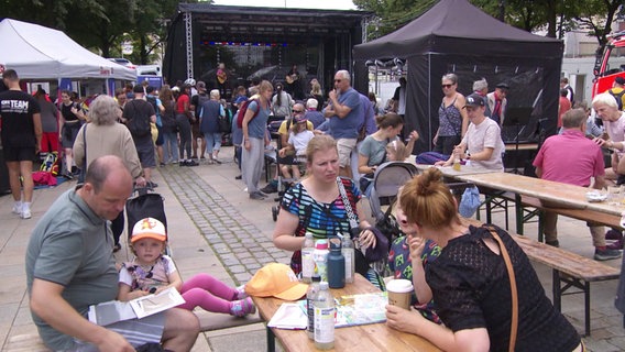 Auf einem Platz sind eine Bühne, Pavillons und Tische aufgebaut, and denen sich Familien mit Kindern, Besucherinnen und Besucher tummeln. © Screenshot 