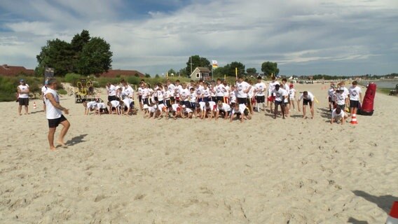 Eine große Gruppe Kinder und Jugendlicher beim Footballtraining am Strand. © Screenshot 