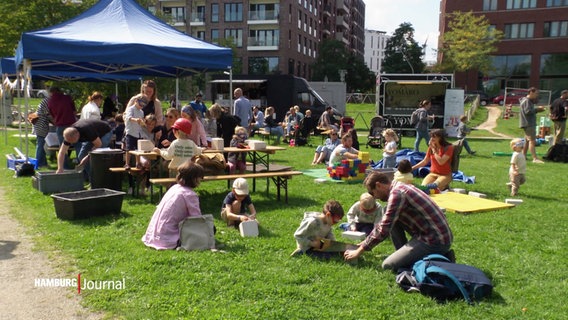 Kinder und Erwachsene sitzen bei einem Fest auf Bänken und dem Rasen © Screenshot 