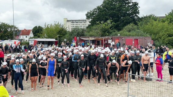 Triathletinnen und Triathleten stehen am Strand an der Startlinie. © Screenshot 