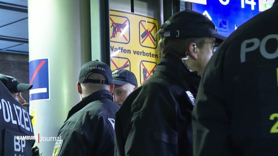 Ein Schild mit der Aufschrift "Waffen verboten!" am Hamburger Hauptbahnhof. Davor Polizeibeamte. © Screenshot 