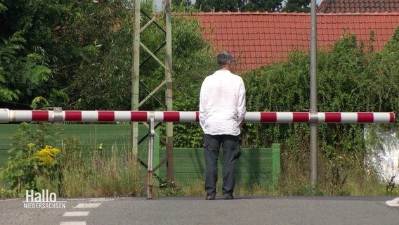 Ein Mann wartet vor einem Bahnübergang. © Screenshot 