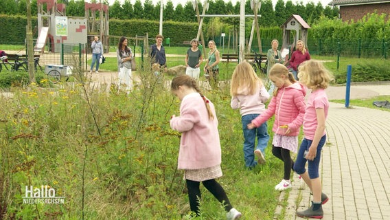 Im Vordergrund stehen Kinder an einer Blühwiese. Im Hintergrund stehen die Mütter. © Screenshot 