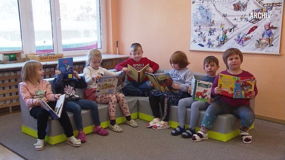 Kinder sitzen mit Büchern in einer Sitzecke in einer Kita. © Screenshot 