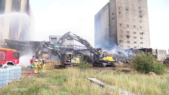 Lösch- und Aufräumarbeiten mit Feuerwehrfahrzeugen und Baggern auf einem qualmendem Industriegelände © Screenshot 