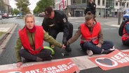 Sitzblockade der Letzten Generation auf einer Straße in Rostock. © Screenshot 