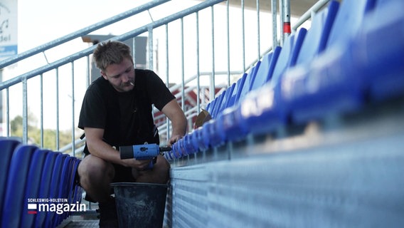 Eine Person befestigt Sitze im Stadion. © Screenshot 