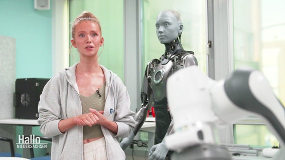 Sandra Drolshagen im Interview. Neben ihr steht ein humanoider Roboter. © Screenshot 