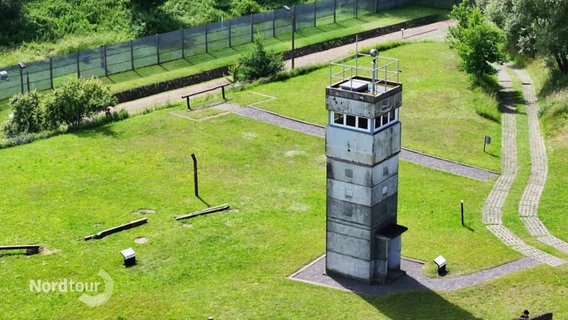 Innerdeutsche Grenze: Ein Wachturm steht auf einer Wiese, im Hintergrund ist der Grenzzaun zu sehen. © Screenshot 